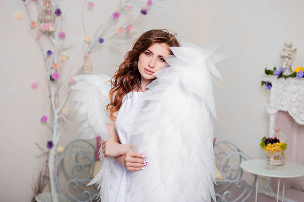 Portrait of a young woman, an angel in a white dress stands wrapped in wings. - 写真・画像