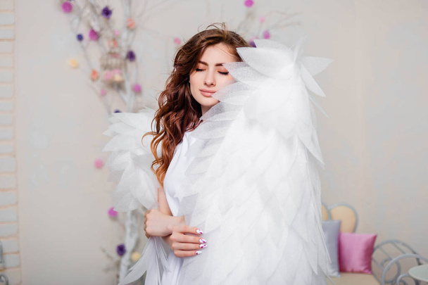 Portret van een jonge vrouw, een engel in een witte jurk staat gehuld in vleugels. - Foto, afbeelding