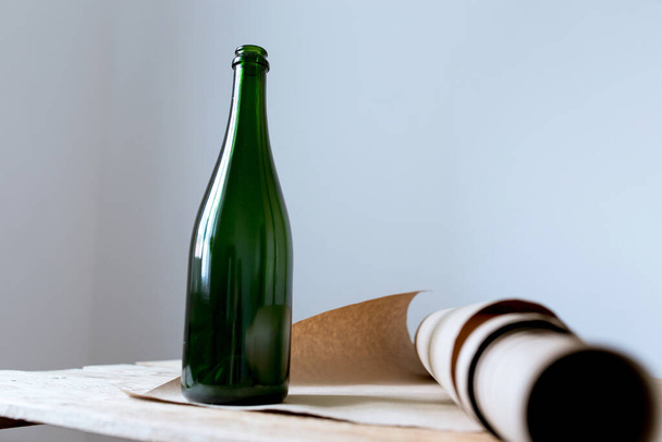 grüne Flasche auf einem Holztisch mit einer Rolle Bastelpapier auf weißem Hintergrund im Inneren - Foto, Bild