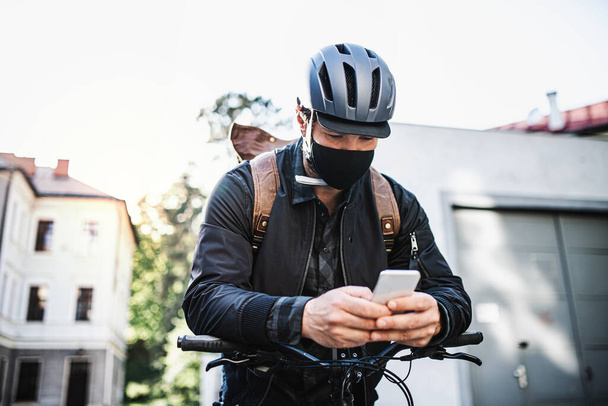 Delivery man courier with face mask and bicycle using smartphone in town. - Foto, immagini
