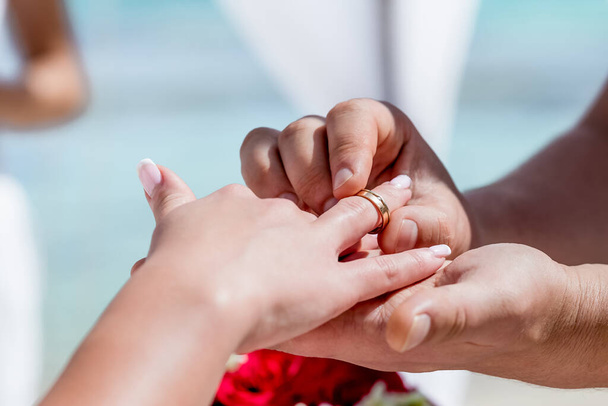 Bride and groom exchanging wedding rings close up during symbolic nautical decor destination wedding marriage on sandy beach in front of the ocean in Punta Cana, Dominican republic   - Foto, Imagen
