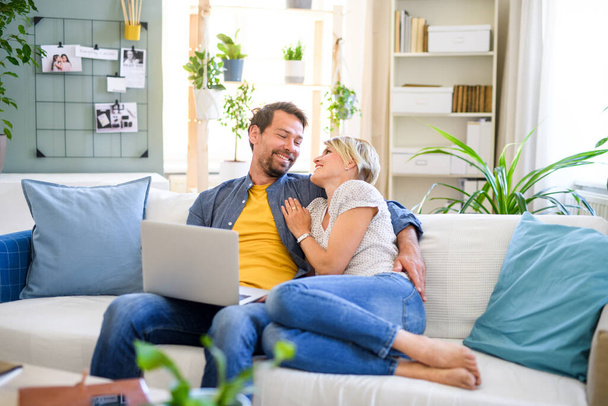 Happy couple in love sitting indoors at home, using laptop. - Φωτογραφία, εικόνα