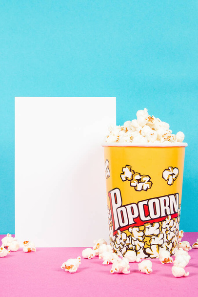 Gelbe Schachtel mit frischen Popcorn auf rosa und blauem Hintergrund - Foto, Bild