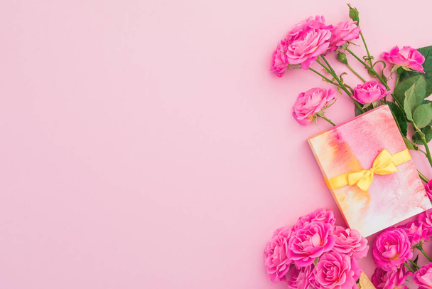 Kwiatowa ramka z kwiatami róż i pudełko prezentowe na różowym tle. Płaskie położenie, widok z góry, - Zdjęcie, obraz