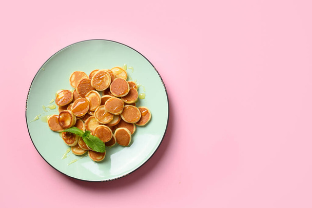 Homemade tiny cereal pancakes with honey in green plate on pink background. View from above. Tasty breakfast. - Photo, image