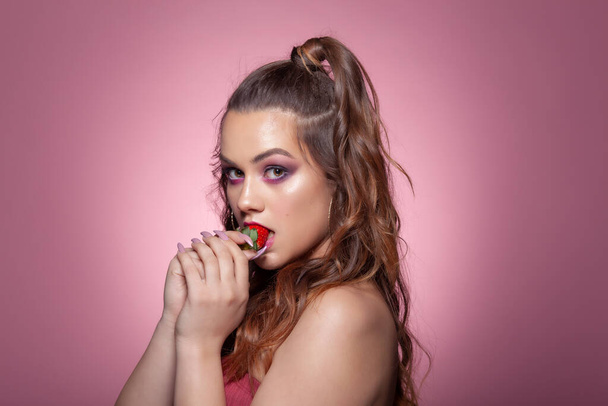 Joven mujer sexy comiendo fresa. Estudio rodaje sobre fondo rosa
. - Foto, imagen