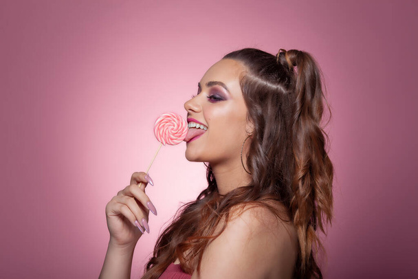 Νεαρή σέξι γυναίκα τρώει γλειφιτζούρι. Στούντιο σουτ σε ροζ φόντο. - Φωτογραφία, εικόνα