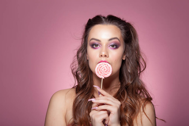若いセクシーな女性はロリポップを食べています。スタジオ撮影ピンクの背景. - 写真・画像