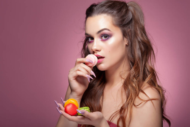 Young sexy woman eating color macarons candies. Studio shoot on pink background. - Valokuva, kuva