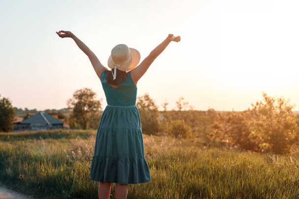 happy young woman at summer sunset in the field raises her hands to the sky. the concept of freedom, rest, summer, nature, happiness, harmony - Fotoğraf, Görsel