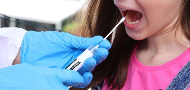 swab for the detection of the corona virus on the mouth of the young Caucasian girl - Photo, Image