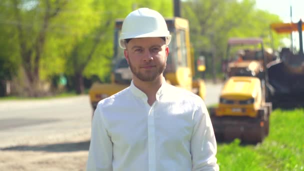 Manager of the repair works in a white helmet on the background of special road equipment - Imágenes, Vídeo