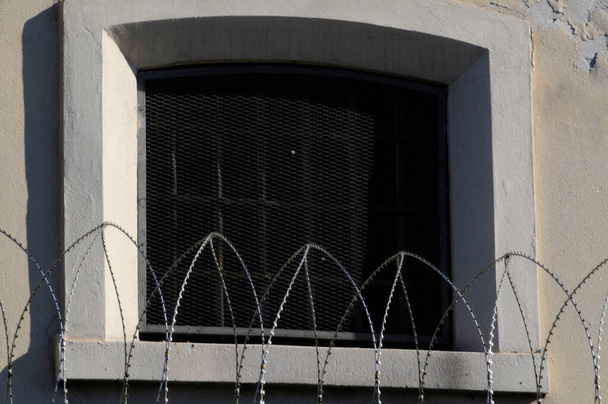 Hapishane penceresi dışarıdan, önünde dikenli tel var. - Fotoğraf, Görsel