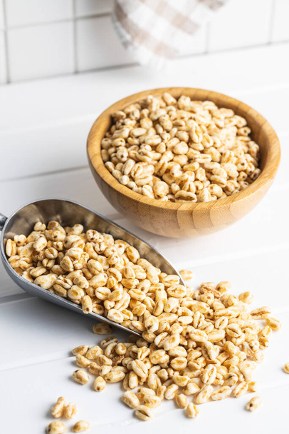 Puffed wheat covered with honey in scoop. Cereal breakfast on kitchen table. - Foto, afbeelding