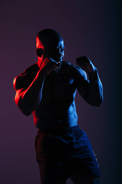 Advertising shot Boxer African American in profile with a naked torso box on a blue neon background. - Photo, Image