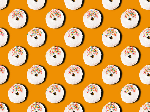 Dessert coloré motif sans couture de beignets avec glaçage blanc et garniture de pâte à sucre multicolore sur fond orange. Vue du dessus
 - Photo, image