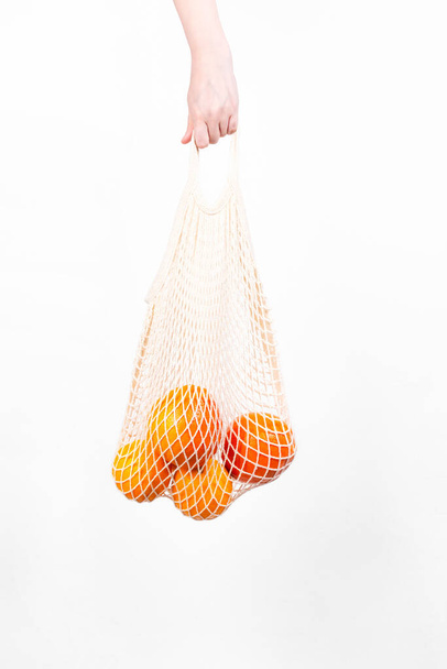 Woman's hand is on hold string bag with oranges and grapefruits. Concept zero waste, eco-friendly - Fotoğraf, Görsel