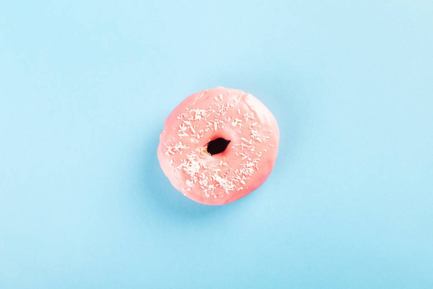 Donut with pink icing and coconut pastry topping on blue background. Top view - Photo, image