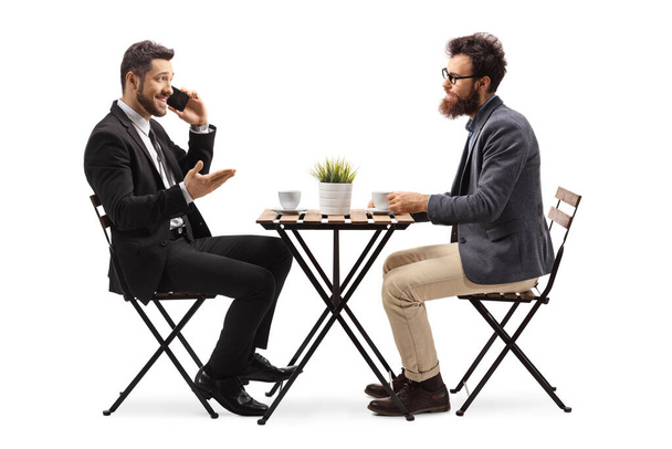 Бізнесмен розмовляє на мобільному телефоні і сидить за журнальним столиком з другом ізольовано на білому тлі
 - Фото, зображення