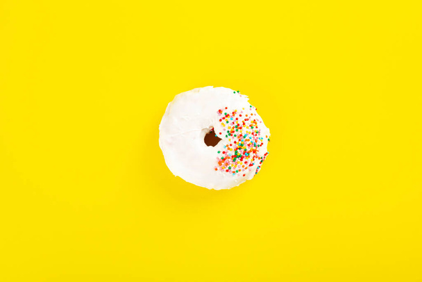 Donut with white icing and multicolored sugar pastry topping on yellow background. Top view - Foto, immagini