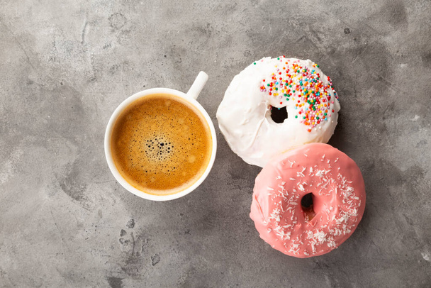 White cup of coffee and donut in white and pink icing and multicolored sugar pastry topping on grey background. Top view - Valokuva, kuva