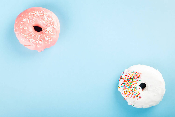 Donut with white and pink icing and multicolored sugar pastry topping on blue background. Top view. Copy space - Foto, Imagem