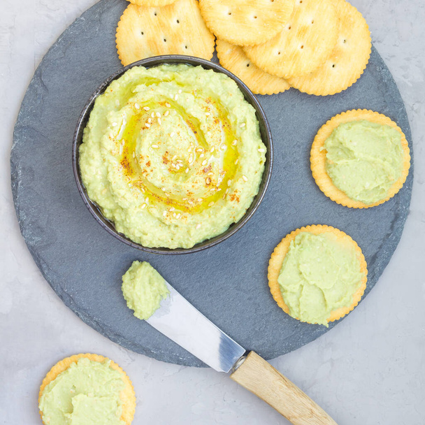 Avocado hummus sprinkled with olive oil, paprika and sesame, served with crackers, top view, square format - Foto, Bild