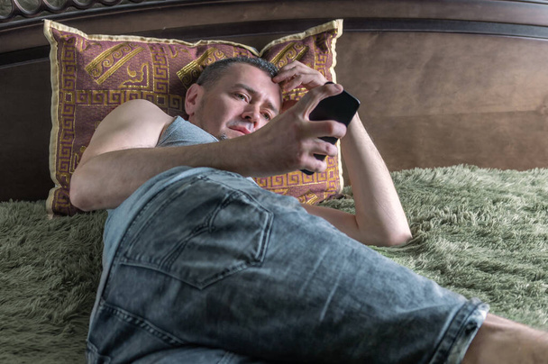 mężczyzna na łóżku z telefonem za pomocą aplikacji lub czytania wiadomości - Zdjęcie, obraz
