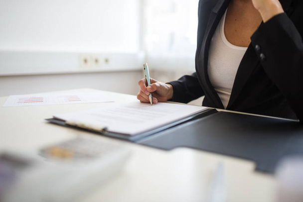 Vista de cerca de la mujer de negocios sentada en su escritorio firmando un documento o contrato en una carpeta
. - Foto, Imagen