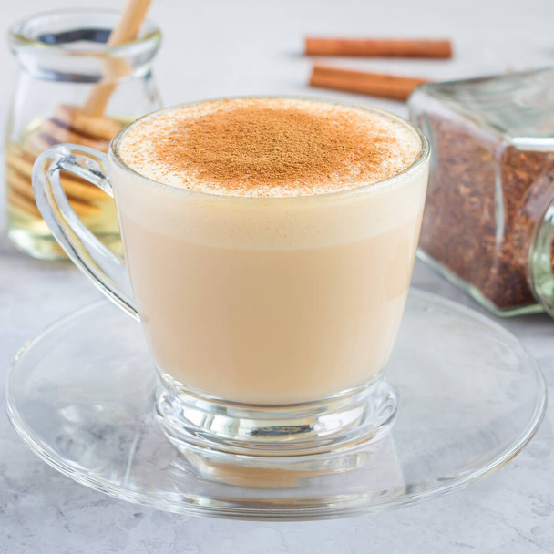 Healthy rooibos red tea latte topped with cinnamon, in glass cup and ingredients on background, square - 写真・画像