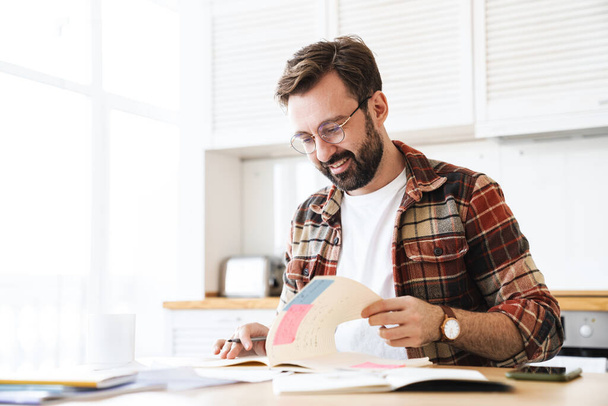 Portrait of excited bearded man wearing eyeglasses smiling while working with notes at home - Fotoğraf, Görsel