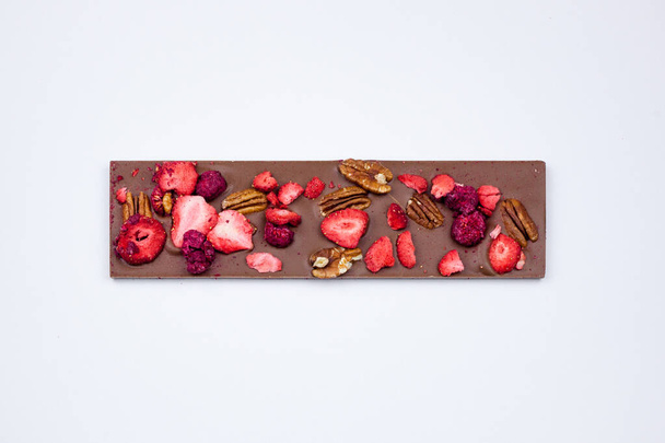 Chocolate bar with nuts, dried strawberries and raspberries on white background. - Fotó, kép