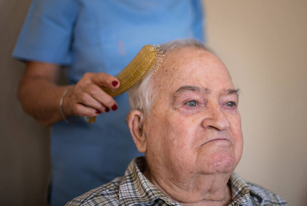 Enfermera está cepillando el cabello de un hombre mayor con un peine, concepto de cuidado en casa con una enfermera
 - Foto, Imagen