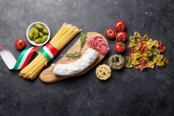 Italian cuisine food ingredients. Pasta, cheese, salami, olives and tomatoes. Top view flat lay on stone table with copy space - Фото, зображення