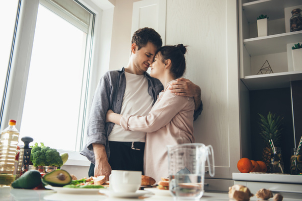 Charmant couple caucasien dans la cuisine embrassant tout en préparant la nourriture ensemble
 - Photo, image