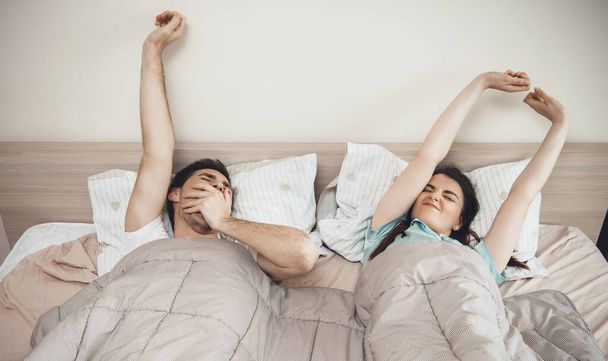 Caucasian couple getting up in the morning stretching arms and yawning - Фото, зображення