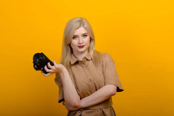 Porträt eines blonden Mädchens mit einer Kamera in der Hand auf gelbem Hintergrund. Abgeschlossenes Studio. - Foto, Bild