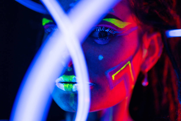 Portrait of a Girl with Glowing Tubes in Neon UF Light. Model Girl with Dreadlocks and Fluorescent Creative Psychedelic MakeUp, Art Design of Female Disco Dancer Model in UV, Colorful Abstract Make-Up - Foto, immagini
