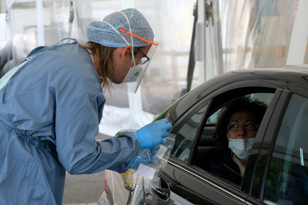 Een gezondheidswerker voert op 5 mei 2020 een coronavirustest uit op een drive-through locatie in het Universitair Ziekenhuis van Luik in België. - Foto, afbeelding