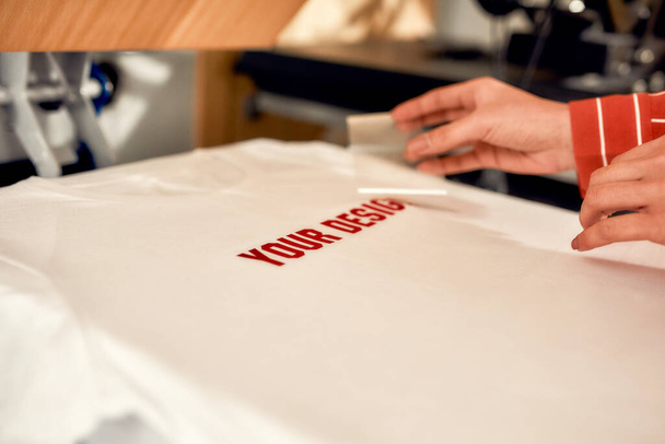 We bring print to life. Cropped shot of hand of woman removing the backing from advertisement sticker with text while putting it on a T-Shirt - Fotografie, Obrázek