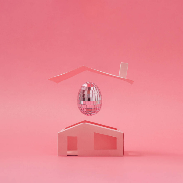 最小限の家の上にピンクのディスコボールイースターエッグ。イースター休暇の創造的な概念の背景. - 写真・画像