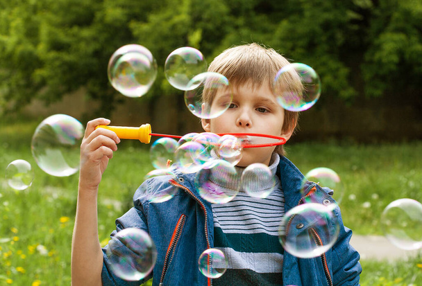 Little cute boy pompuje bańki mydlane w parku w naturze, radosne emocje u dziecka, jasne duże kule mydlane. - Zdjęcie, obraz