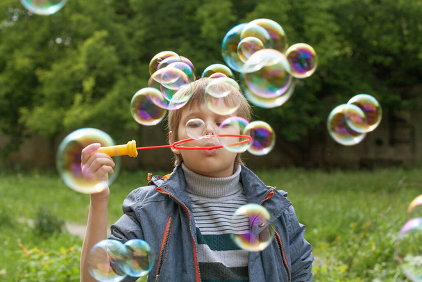 Little cute boy inflates soap bubbles in the park in nature, joyful emotions in a child, bright big soap balls. - Photo, Image