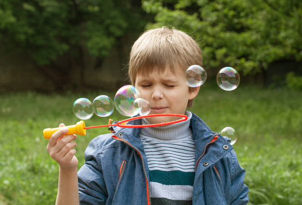 Pequeño niño lindo infla burbujas de jabón en el parque en la naturaleza, emociones alegres en un niño, bolas de jabón grandes brillantes. - Foto, imagen