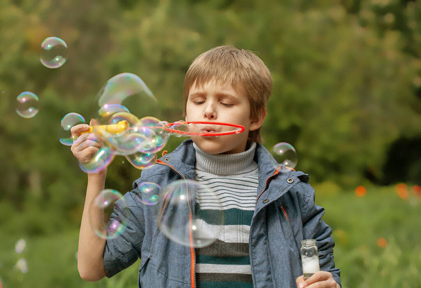 Kleiner süßer Junge bläst Seifenblasen im Park in der Natur auf, fröhliche Gefühle im Kind, helle große Seifenkugeln. - Foto, Bild