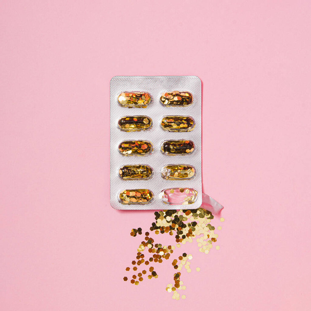 Concepto creativo con píldoras de brillo dorado sobre fondo rosa pastel. Mínimo plano lay
, - Foto, Imagen