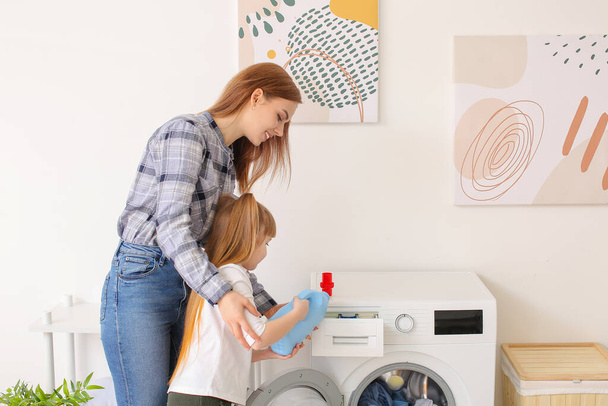 Η γυναίκα και η κορούλα της κάνουν μπουγάδα στο σπίτι. - Φωτογραφία, εικόνα