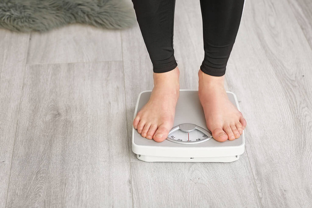 Молода жінка вимірює свою вагу вдома
 - Фото, зображення