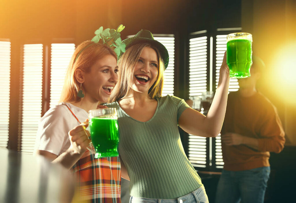 Young women with glasses of green beer in pub. St. Patrick's Day celebration - Φωτογραφία, εικόνα