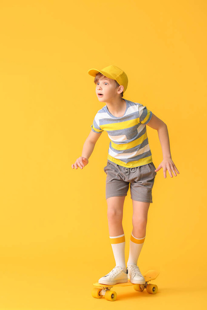 Sporty little boy with skateboard on color background - Фото, изображение